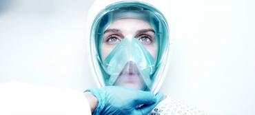 A futuristic mask is placed on a woman by a medic in a white environment